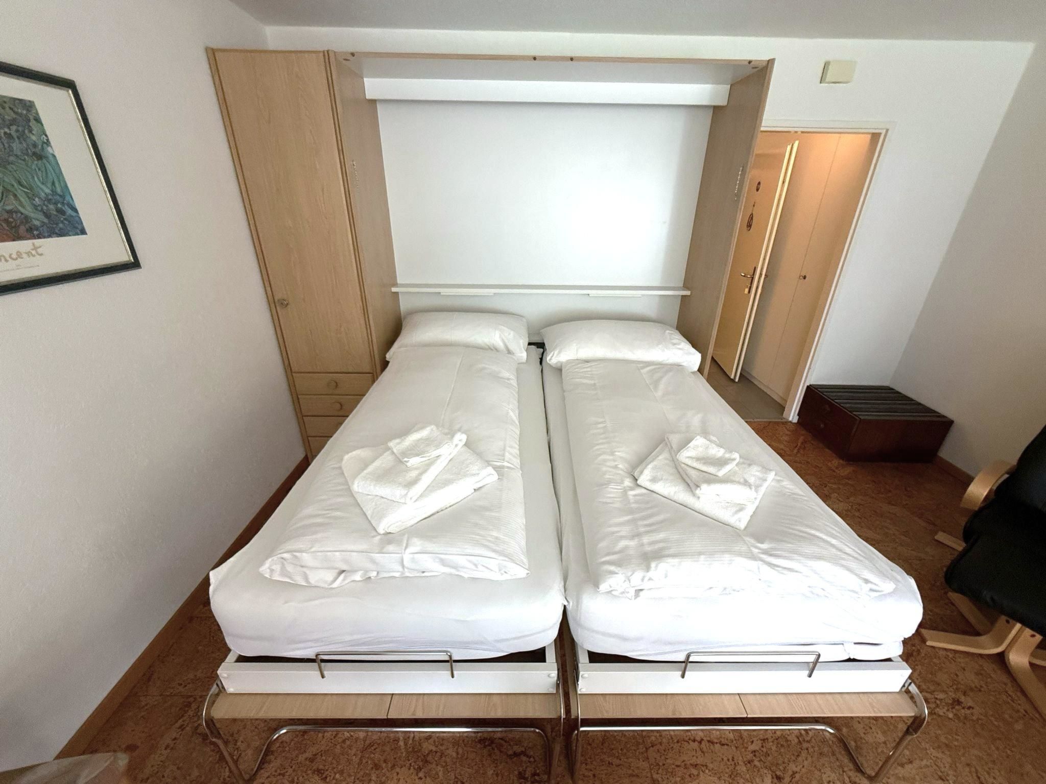A twin room with two beds, a wooden wardrobe, a framed picture on the wall, and a small table.