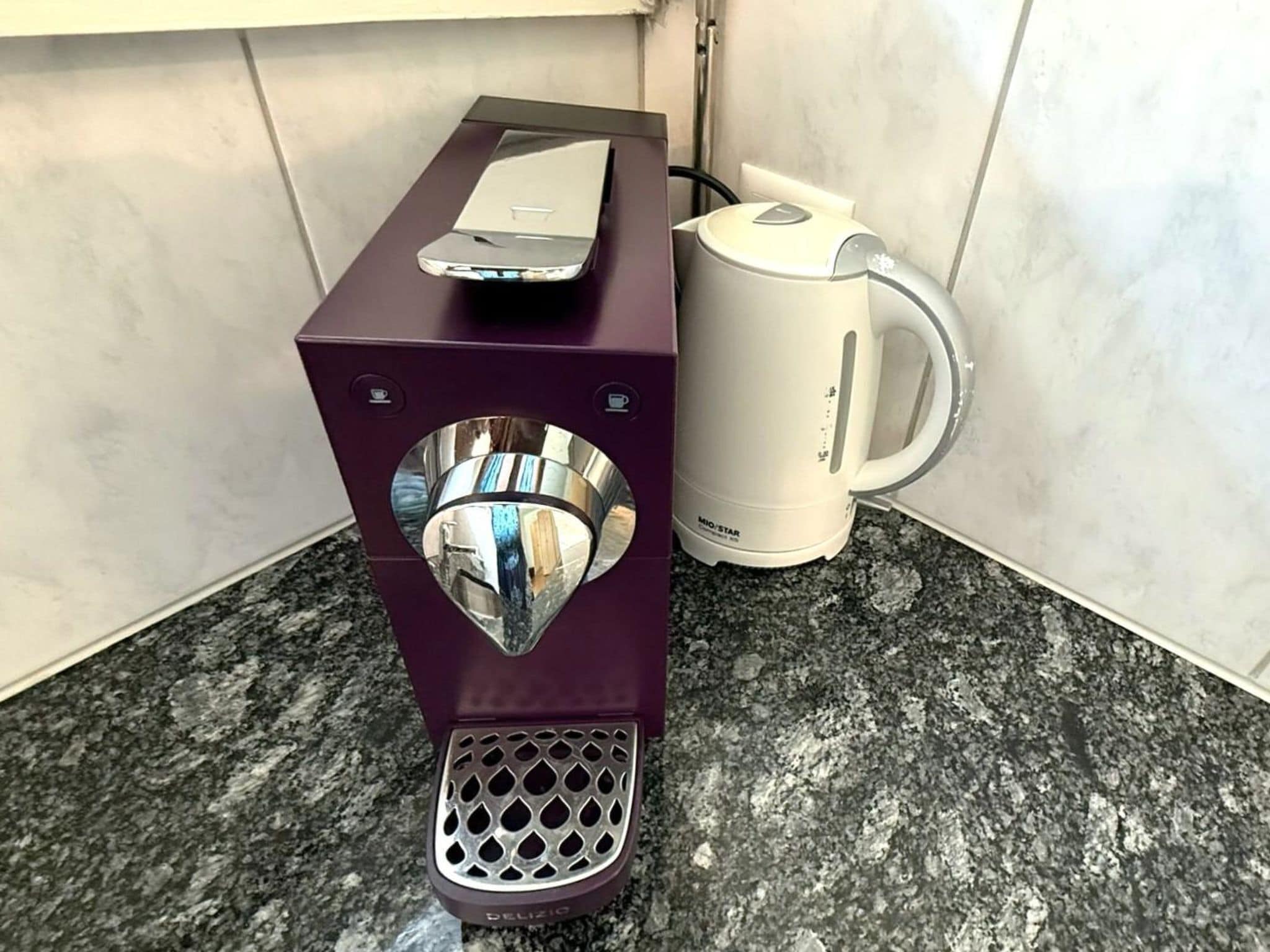 Une machine à café dotée d’un réservoir d’eau et d’une verseuse, posée sur un comptoir en granit.
