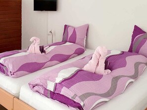 Ein Doppelbett mit gemustertem Bettbezug, ein Flachbildfernseher an der Wand und ein Holz-Kopfteil.