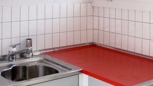 Ett kök med vita kakelväggar, en diskho i rostfritt stål och en röd bänkskiva.