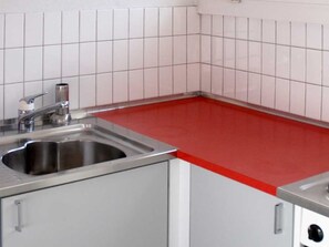 Eine Küche mit weißen Fliesen, einer Edelstahl-Spüle und einer roten Arbeitsplatte.