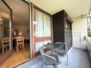 Un balcon avec une table et des chaises, une porte-fenêtre coulissante donnant sur une pièce et une vue sur l’extérieur.