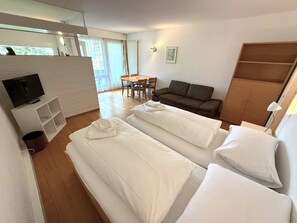 Une chambre d’hôtel avec deux lits, une télévision, une table à manger avec des chaises, un canapé et une armoire.