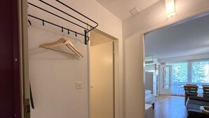 Käytävässä on puinen naulakko, ovi, joka johtaa huoneeseen, ja näkymä ruokailutilaan, jossa on pöytä ja tuoleja.