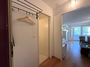 A hallway with a wooden hanger rack, a door leading to a room, and a view into a dining area with a table and chairs. - Fortuna 113 # 2-bed apartment, Dusche, WC 2-Bettwohnung, Dusche, WC by Interhome (Leukerbad)