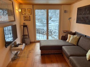 A cozy living room with a sofa, a television, and a window with a view of a snowy landscape. - Edelweiss B 41 # 4-bed apartment, Dusche und Bad, WC by Interhome (Leukerbad)