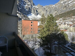 Une vue sur une montagne avec des sommets enneigés, un bâtiment rouge et un pin au premier plan.