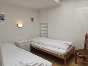 A small, clean room with two single beds, a nightstand, a chair, and a wall-mounted light. - Fortuna 316 # 5-bed apartment, Dusche, WC 5-Bettwohnung, Dusche, WC by Interhome (Leukerbad)