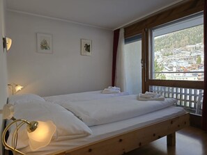 Un lit simple avec du linge de lit blanc, une lampe de chevet et deux tableaux encadrés accrochés au mur.