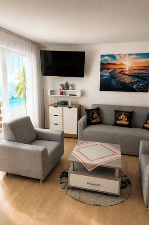 A modern living room with a grey sofa, a grey armchair, a coffee table, and a flat-screen TV mounted on the wall. - Majesta Leukerbad # 2-bed apartment, Dusche, WC by Interhome (Leukerbad)