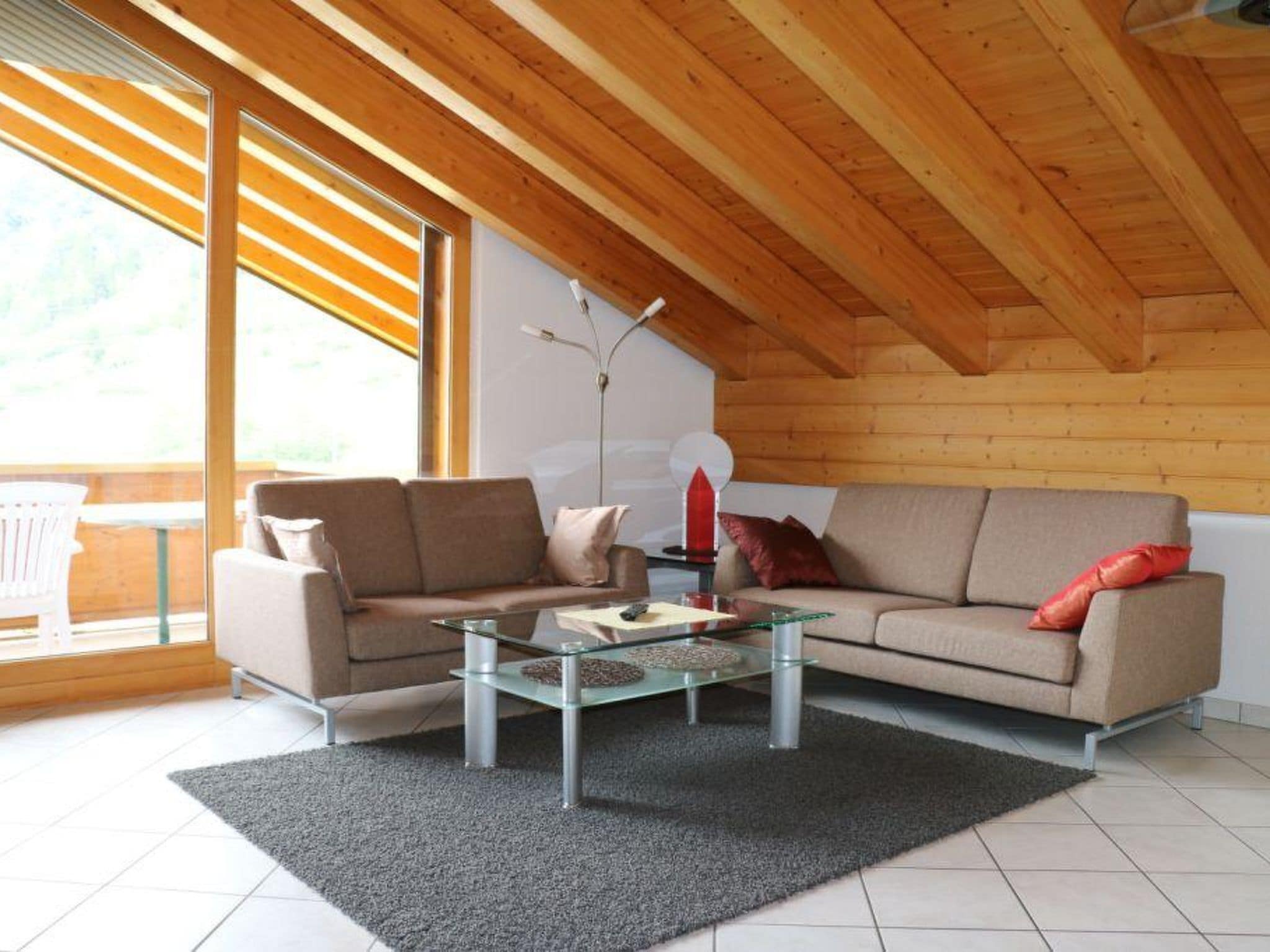 Ett modernt vardagsrum med ett soffbord i glas, en beige soffa och ett träpanelat tak.