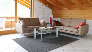 Een moderne woonkamer met een glazen salontafel, een beige bank en een houten plafond.