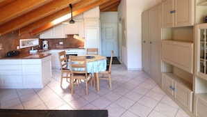 Een keuken met houten balken, witte kasten, een eettafel met stoelen en een betegelde vloer.