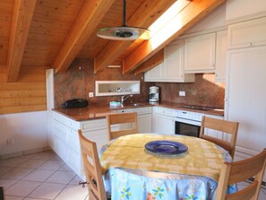 A compact kitchen with wooden beams, white cabinets, a dining table with a floral tablecloth, and a coffee maker. - Bergkristall Leukerbad # 4-bed apartment, Dusche, WC by Interhome (Leukerbad)