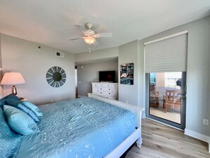 A bedroom with a bed, a ceiling fan, a TV, a dresser, and a view of a balcony with outdoor furniture. - Palisade Palms Beach High Rise (Galveston)