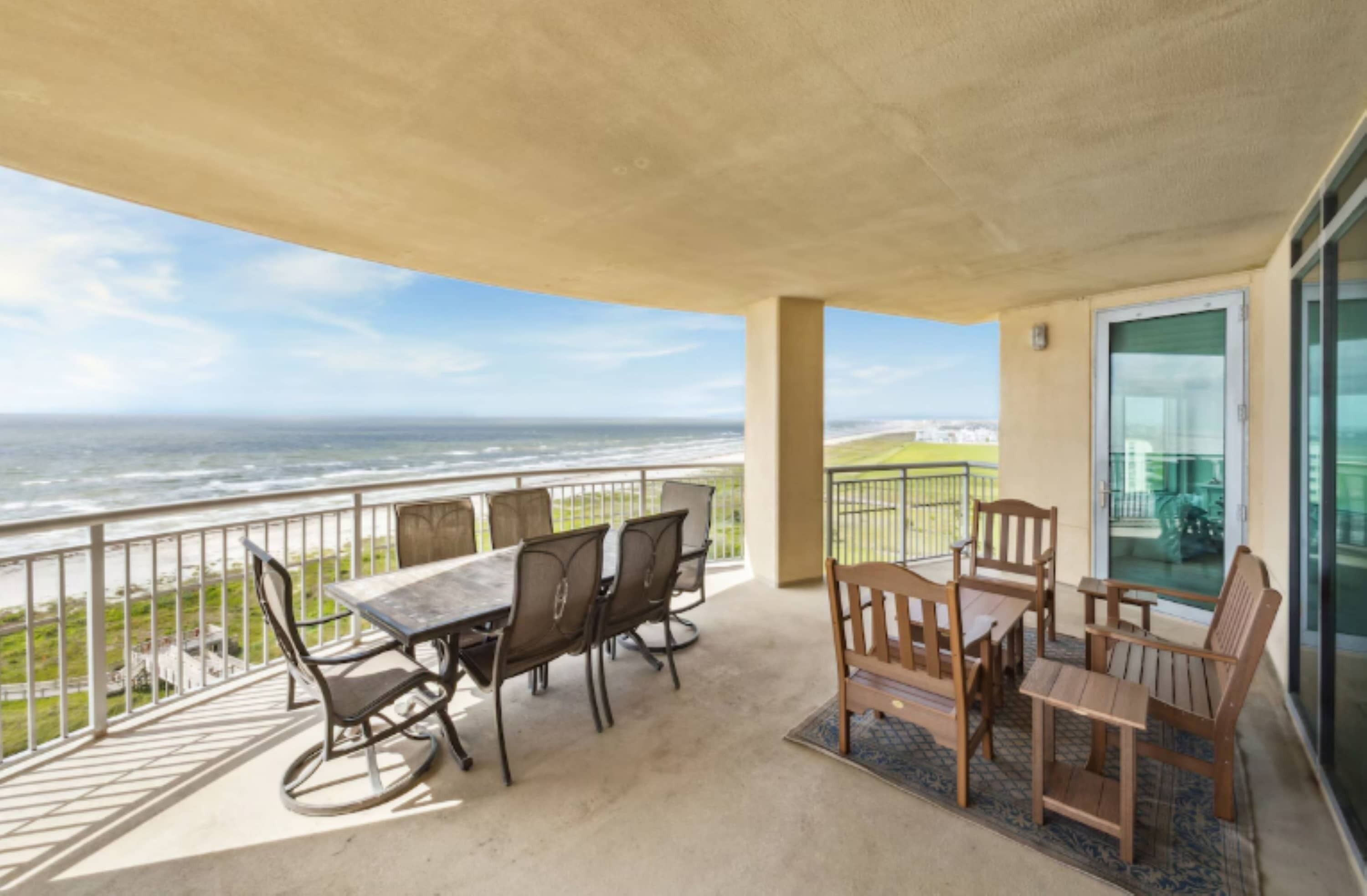 A balcony with a table and chairs, overlooking a coastal view.