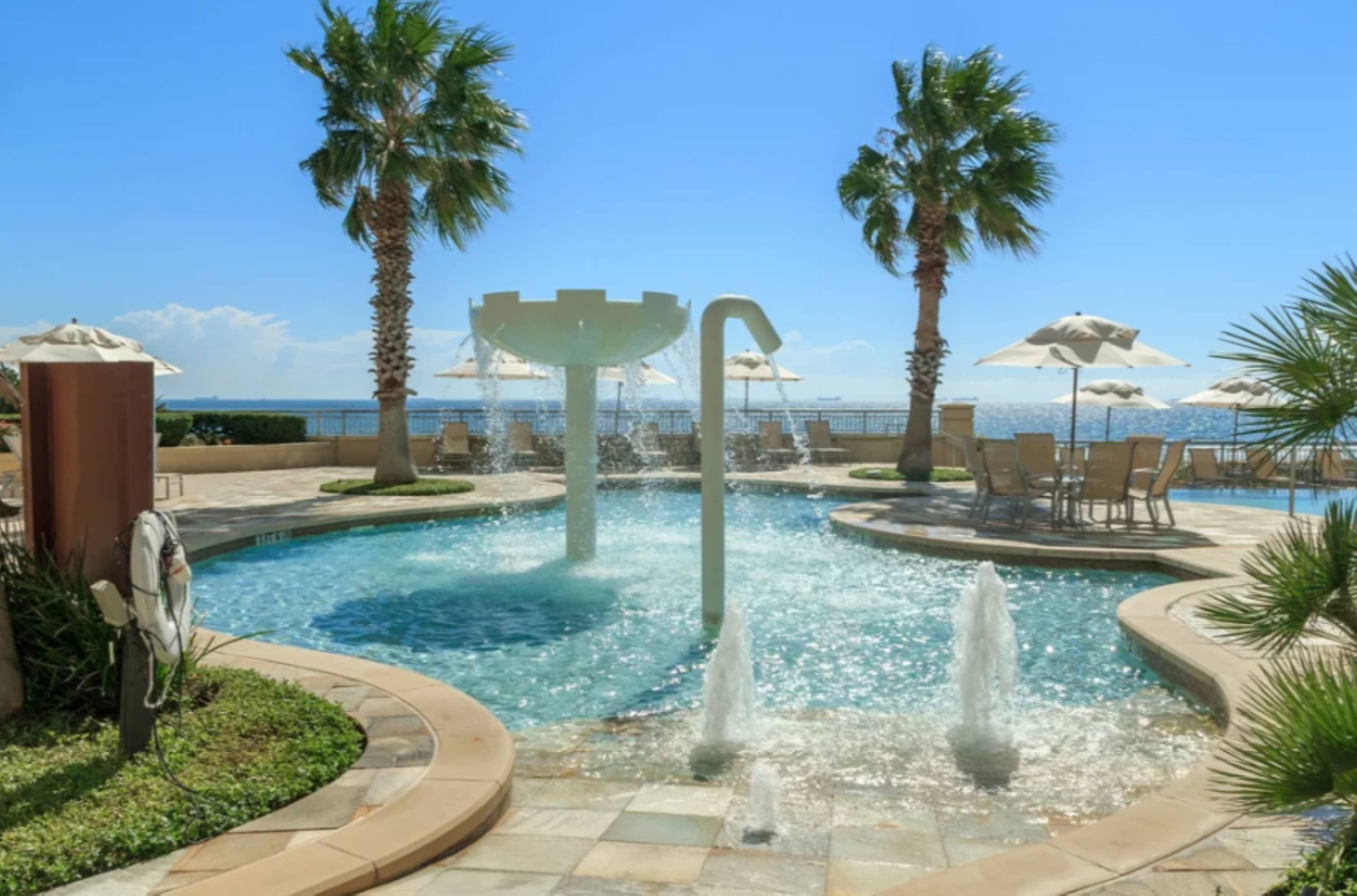 A pool area with palm trees, a fountain, and lounge chairs.