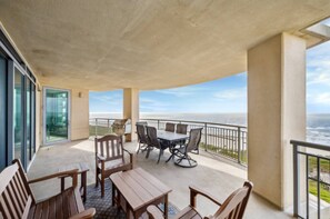 A balcony with a table and chairs, a glass door, and a view of the ocean. - Palisade Palms Beach High Rise (Galveston)