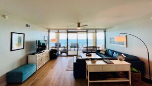 A living room with a sofa, coffee table, TV, and a view of the ocean. - Palisade Palms Beach High Rise (Galveston)