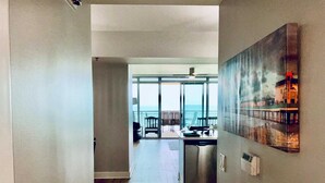 A hallway leading to a balcony with a view of the ocean, a dining area, and a kitchen. - Palisade Palms Beach High Rise (Galveston)