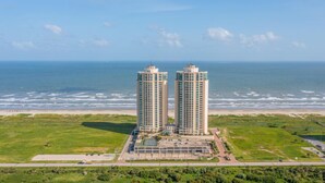 A coastal hotel with two high-rise buildings, a parking area, and a view of the ocean. - Palisade Palms Beach High Rise (Galveston)