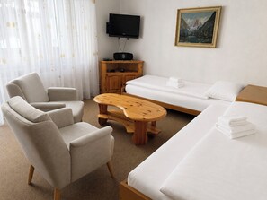 Hotellihuone, jossa on sohva, tuoli, puinen sohvapöytä, sänky, televisio ja taulu seinällä.