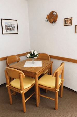 A wooden dining table with four chairs, a vase with flowers, and wall-mounted light fixtures. - Majesta Leukerbad # 2-bed apartment, Dusche, WC by Interhome (Leukerbad)