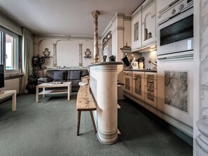 A living room with a sofa, a coffee table, and a bench. There is a large pillar in the center. The room has a fireplace and a kitchen area with cabinets and appliances. - Paradies 507 Appartement/Fewo, Bad, WC, 2-Bettwohnung by Interhome (Arosa)