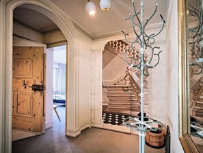 Een gang met een houten deur, een trap met een geruit vloerkleed en een decoratieve metalen constructie.