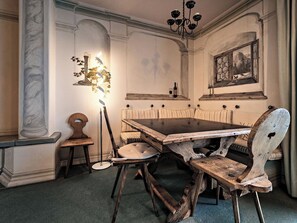 Een eetgedeelte met een houten tafel, stoelen, een kroonluchter en een schilderij aan de muur.