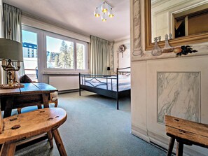 A hotel room with a bed, a table, and a chair. There is a window with a view of trees and buildings. - Paradies 507 Appartement/Fewo,  , 2-Bettwohnung by Interhome (Arosa)