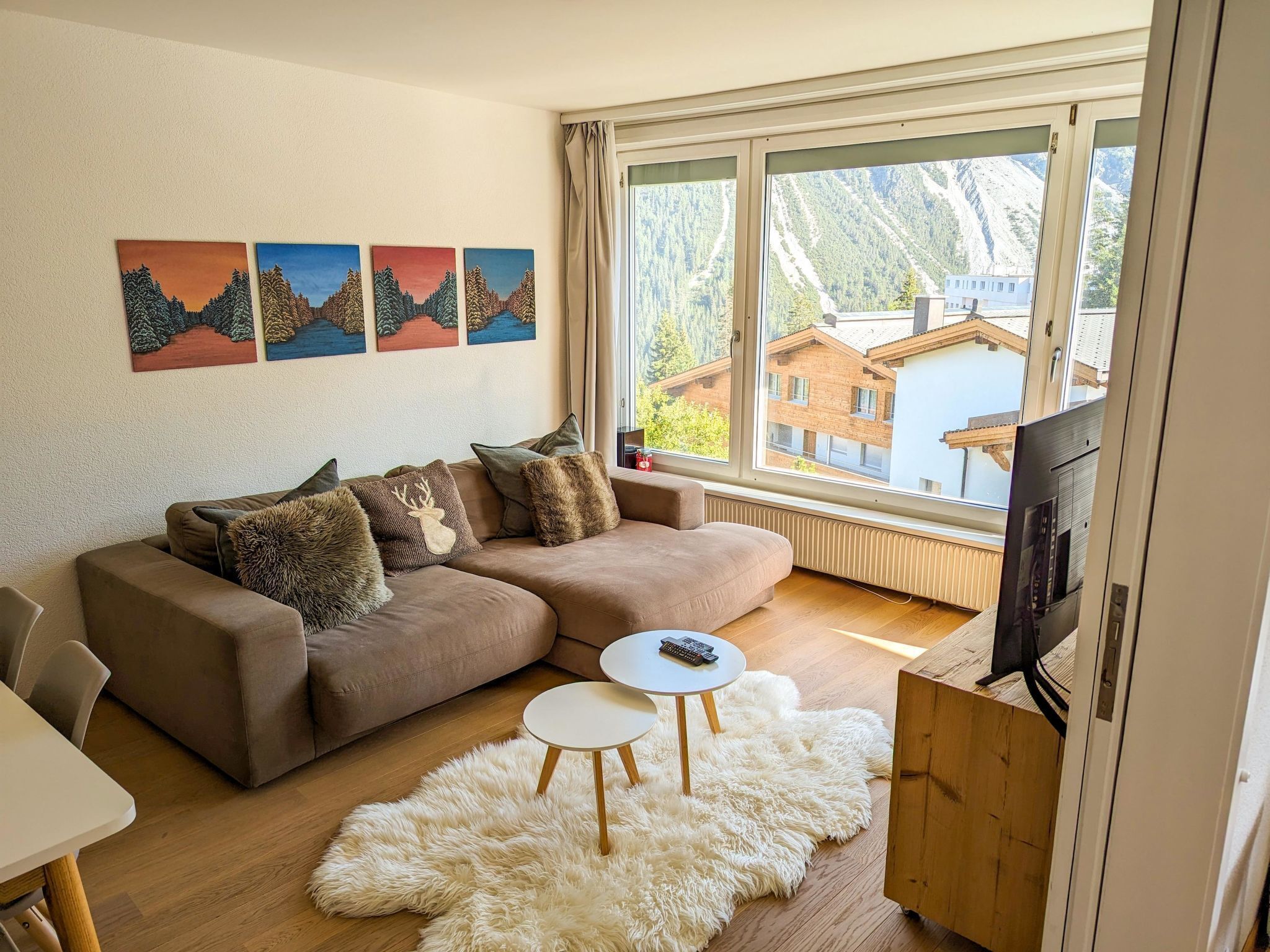 Una sala de estar moderna con un sofá modular, un televisor de pantalla plana y un gran ventanal con vista a las montañas.