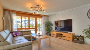 Un salon avec un canapé, un téléviseur, un meuble en bois et de grandes fenêtres.