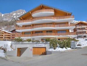Ein mehrstöckiges Hotel mit hölzernen Balkonen, einer Beschilderung mit dem Schriftzug 'Aramis' und einer Bergkulisse.