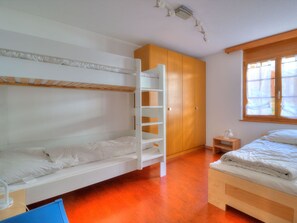Ein Schlafraum mit Etagenbetten, einem Holzschrank, einem Nachttisch und einem Fenster mit Vorhängen.