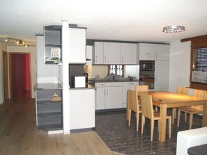 Eine moderne Küche mit weißen Schränken, einem eingebauten Backofen und einem Essbereich mit Holztisch und -stühlen.