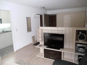 A modern living room with a flat-screen TV, built-in speakers, and a kitchen area visible through an open door. - Valère Leukerbad # 2-bed apartment, Dusche, WC by Interhome (Leukerbad)