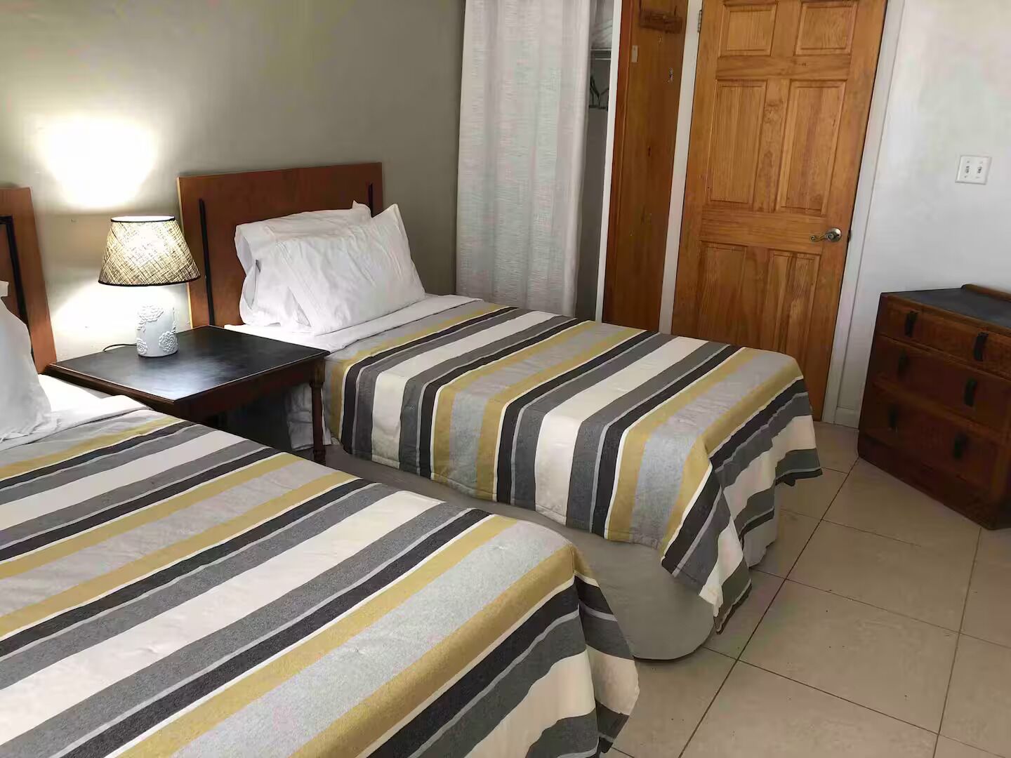 A hotel room with two beds, a nightstand, a lamp, a wooden wardrobe, and a door.