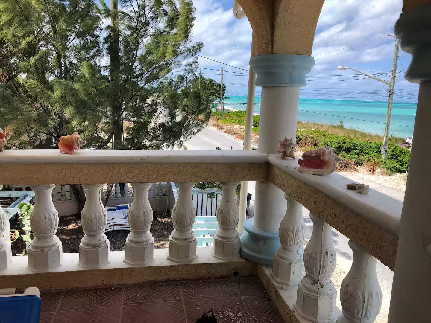 Un balcon avec des balustrades blanches, une vue sur l’océan et une route où circulent des véhicules.