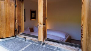 Una habitación con cama, puerta de madera y una ventana pequeña.