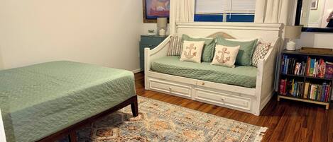 A bedroom with a bed, a sofa bed, a bookshelf, a rug, and a painting on the wall.