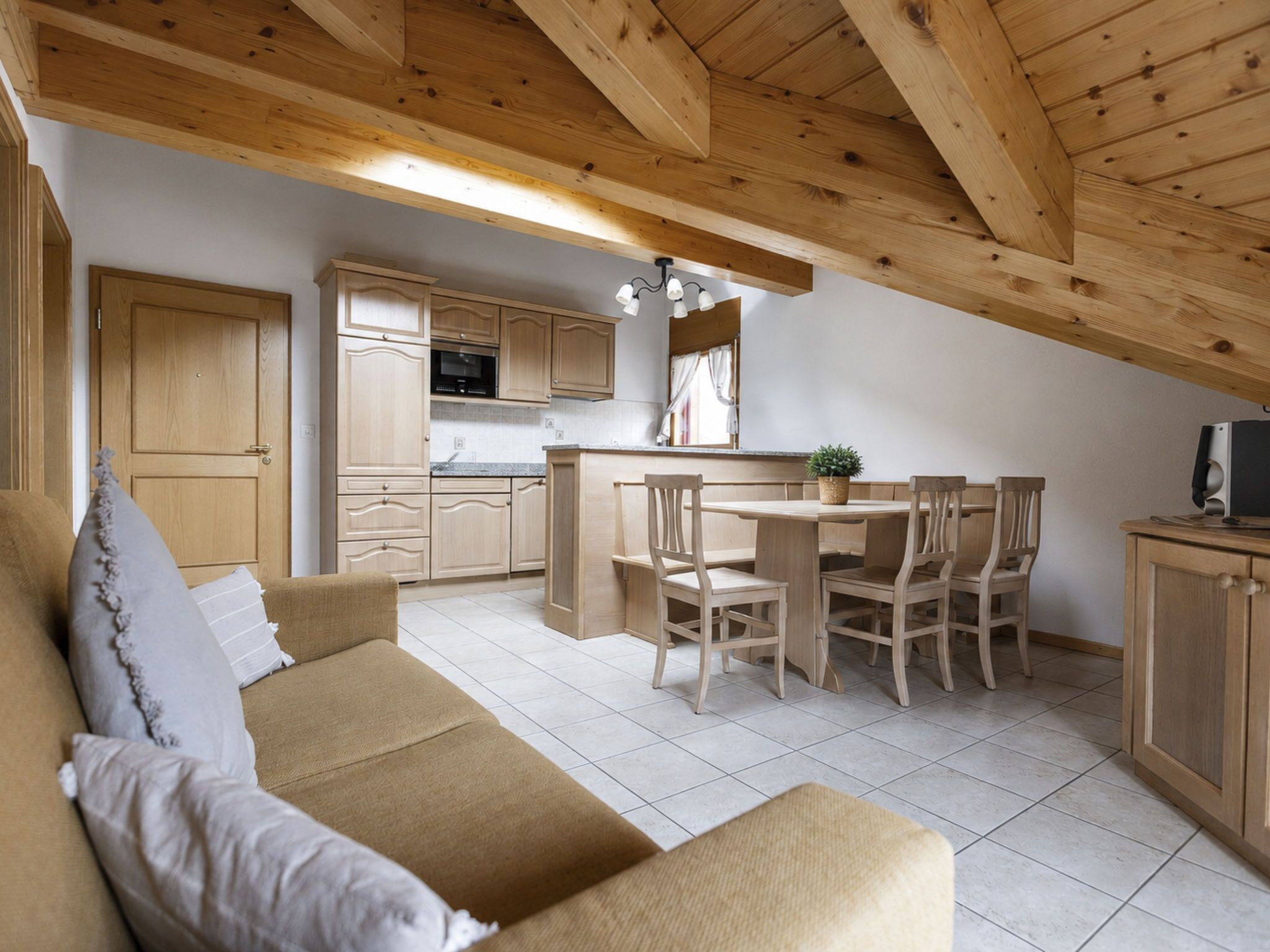 Ein gemütliches Interieur mit einer Couch, einem Esstisch, Stühlen, Holzschränken und einer Küchenzeile.