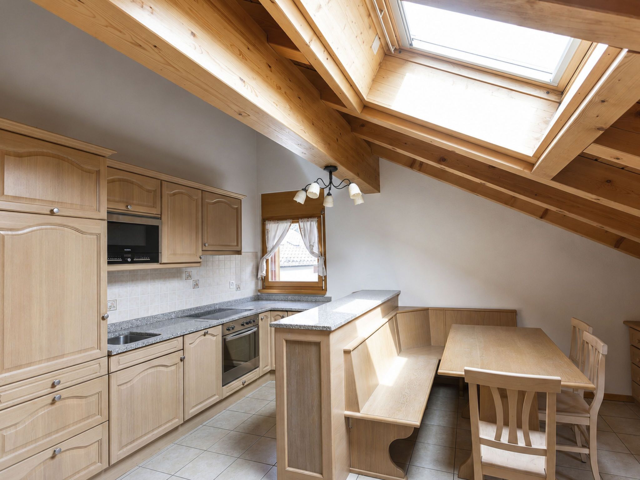 Eine Küche mit Holzausstattung, einer Arbeitsplatte, einem Spülbecken, einem Backofen und einem Essbereich mit einer Bank und Stühlen.