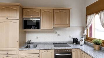 Una cocina con gabinetes de madera, un lavamanos de acero inoxidable, un microondas, un tostador y una ventana con cortinas.