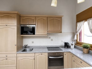 A kitchen with wooden cabinets, a stainless steel sink, a microwave, a toaster, and a window with curtains. - Residenz Château # 3-bed apartment, Bad, WC by Interhome (Leukerbad)