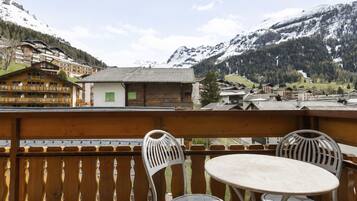 A balcony with two chairs and a table, overlooking a mountainous landscape with buildings.