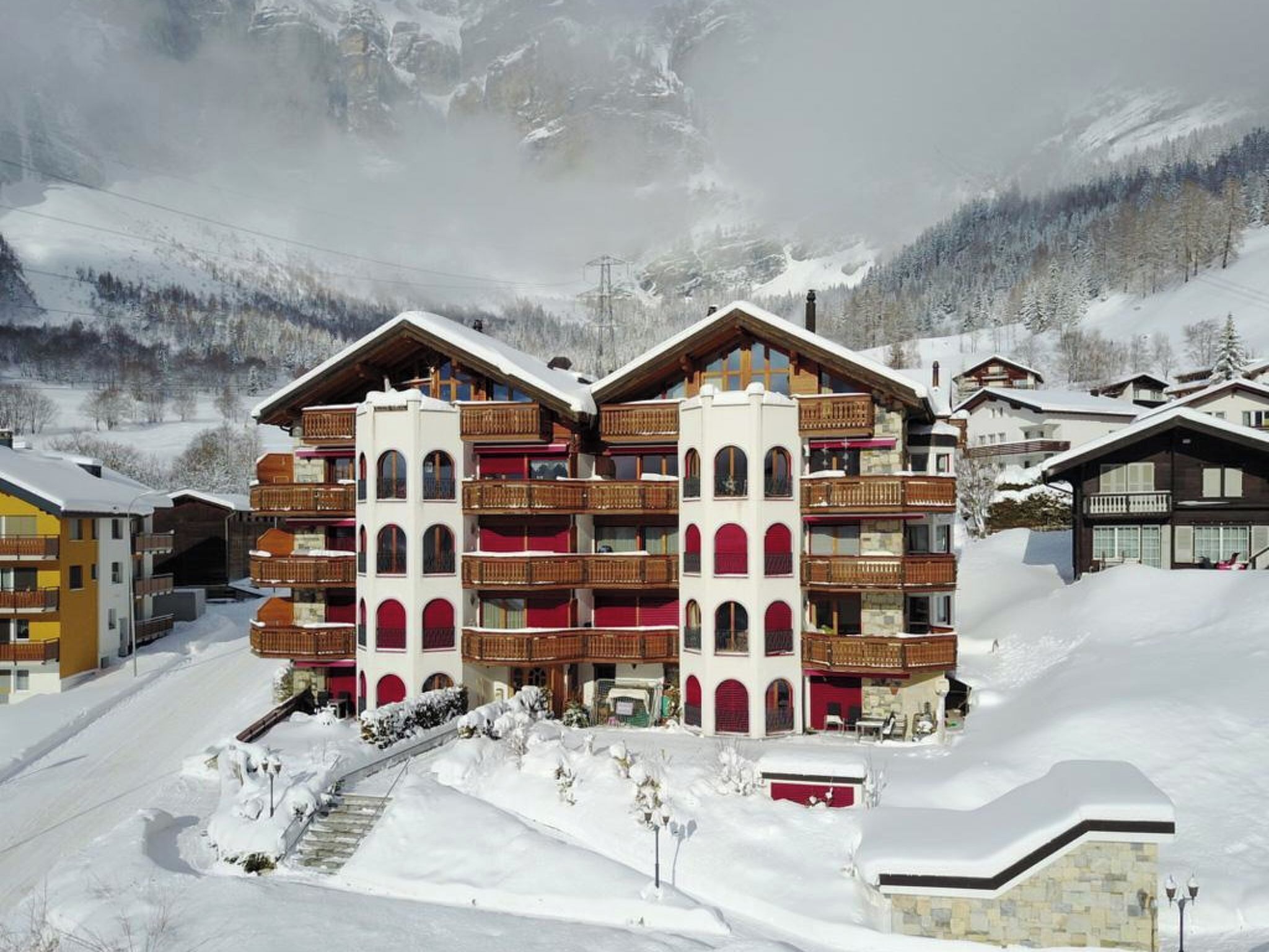 Ein mehrstöckiges Hotel mit Balkonen, im Hintergrund eine Skipiste und eine verschneite Landschaft.