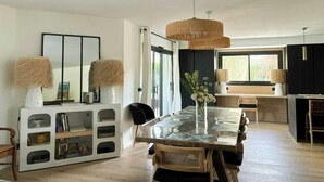 A modern dining area with a glass-top table, woven lamps, and a black cabinet. - Villa with pool near Bassin d'Arcachon (La Teste de Buch)