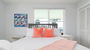 A bedroom with a bed, white walls, a window, a painting, and a nightstand. - Be A Nomad | 2BR Upper Unit | 2 Blocks to Neptune Beach (Neptune Beach)