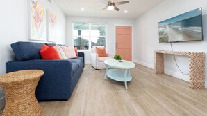 A living room with a sofa, a round table, a television, and a ceiling fan. - Be A Nomad | 2BR Upper Unit | 2 Blocks to Neptune Beach (Neptune Beach)